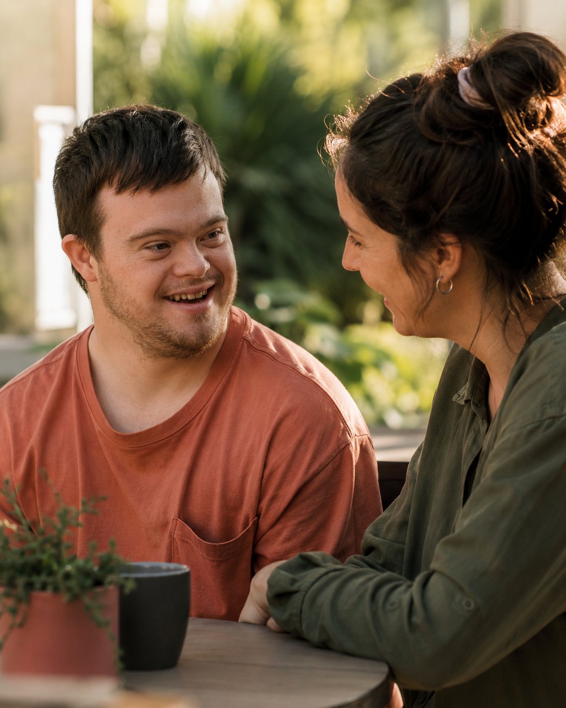 A Northern Star support worker and participant smiling together over coffee in a sunlit outdoor café